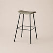 Bar stool with a green seat and black metal legs on a beige background