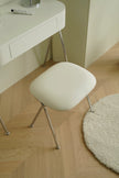 White vanity stool with metal legs in a room with a desk and rug.