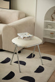 Small white vanity stool with a book on a beige rug in a living room setting.