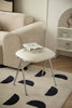 Small white vanity stool with a book on a beige rug in a living room setting.