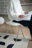 Lady sitting on a vanity chair reading a document in a room with a rug and wall art.