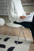 Lady sitting on a vanity chair reading a document in a room with a rug and wall art.