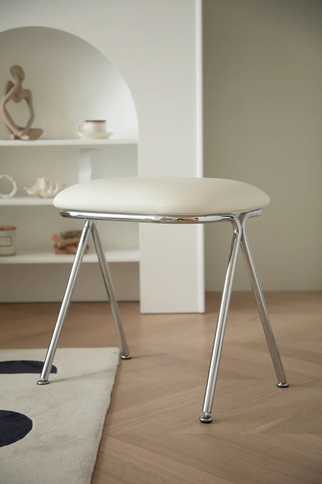 Modern makeup vanity stool with white cushioned seat and metal legs in a minimalistic room.