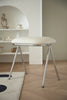 Modern makeup vanity stool with white cushioned seat and metal legs in a minimalistic room.