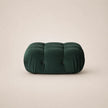 A forest green velvet tufted pouf or ottoman with a rounded rectangular shape, set against a solid light beige background.