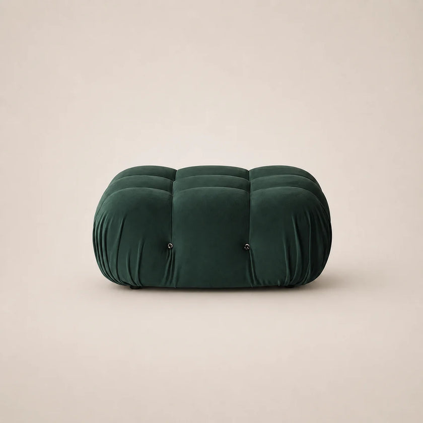 A forest green velvet tufted pouf or ottoman with a rounded rectangular shape, set against a solid light beige background.