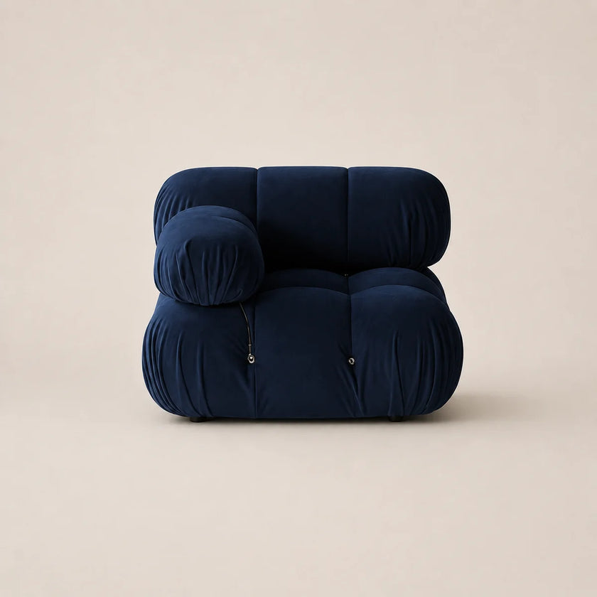 A modern modular floor cushion chair in deep steel blue velvet, featuring a rounded, cloud-like silhouette with zippered pockets, set against a solid warm beige background.