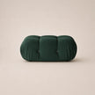 A forest green tufted velvet pouf or bench cushion with a segmented, rounded rectangular shape, set against a solid light beige background.