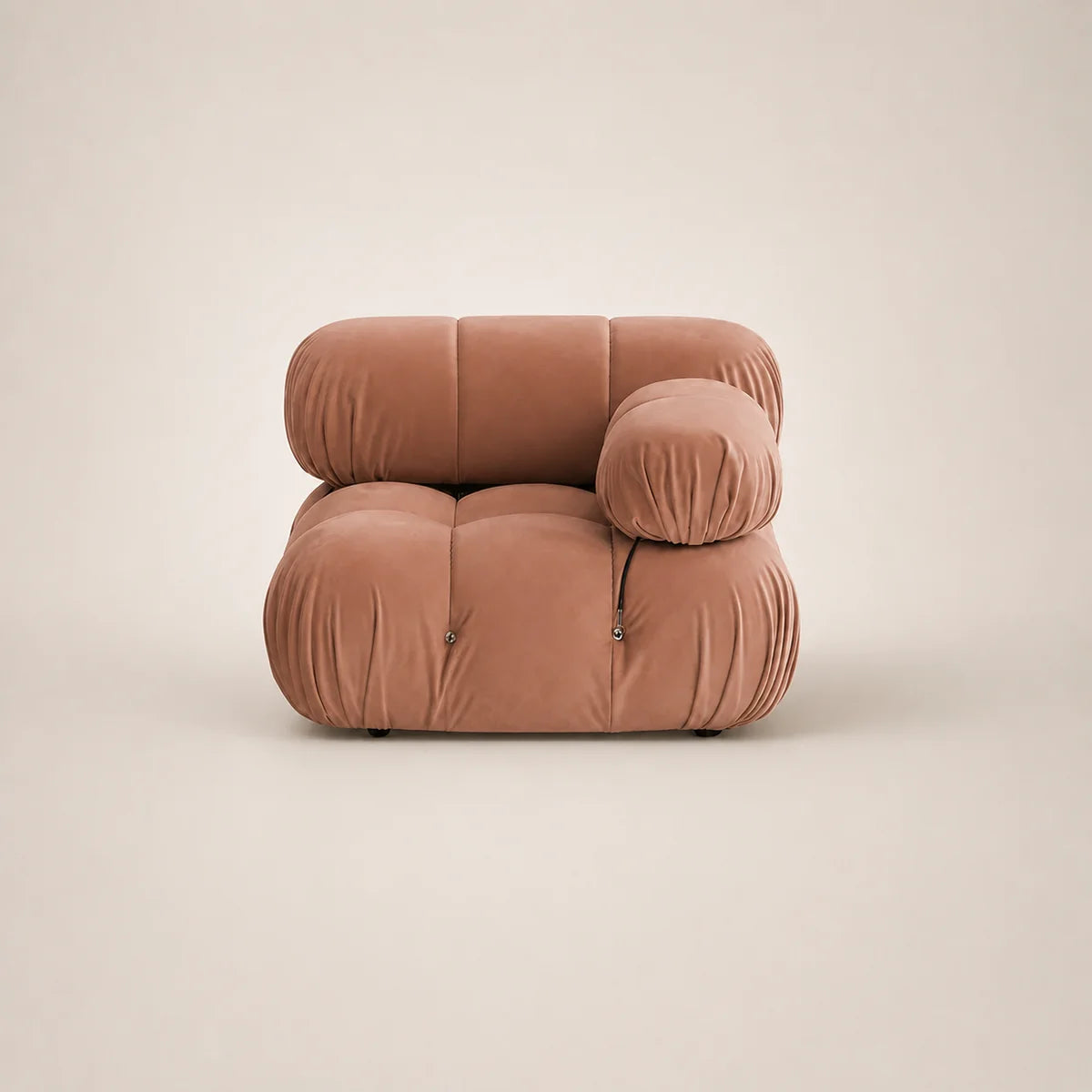 A modern modular lounge chair upholstered in muted pink velvet, featuring a low, rounded blocky silhouette with a separate cylindrical lumbar pillow, set against a solid warm beige background.