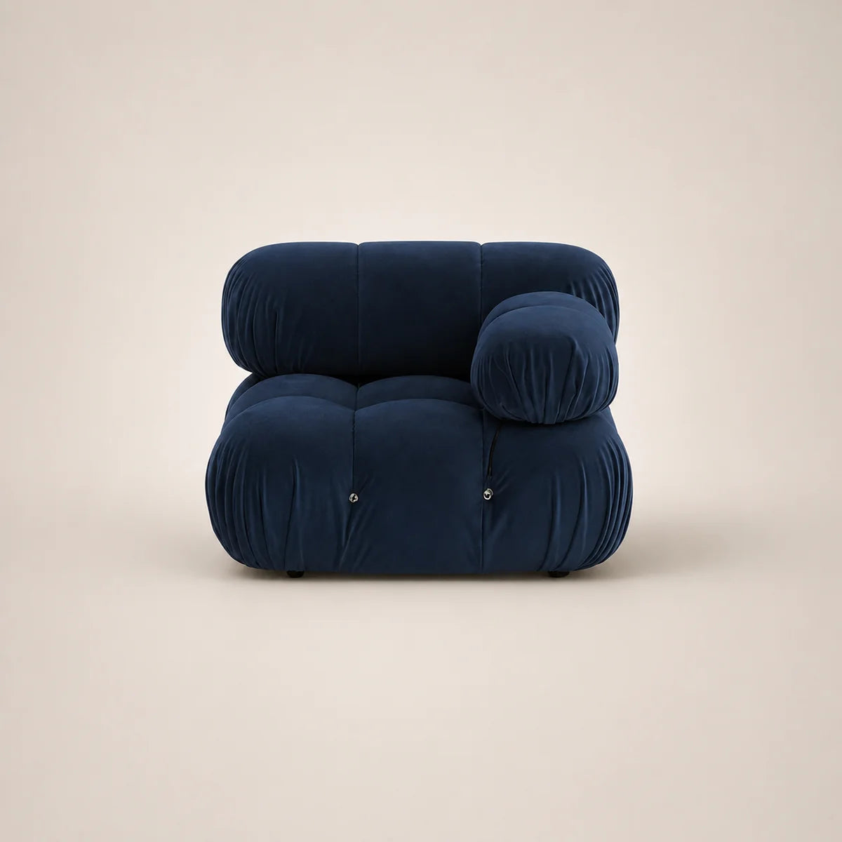 A modern, low-profile modular armchair upholstered in deep steel blue velvet, featuring a rounded, cloud-like silhouette with a separate round back cushion, set against a solid warm beige background.