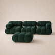 A modern modular sofa set in deep emerald forest green velvet, featuring a low rectangular ottoman in front of a three-seater sofa and two matching armchairs, set against a warm beige studio background.
