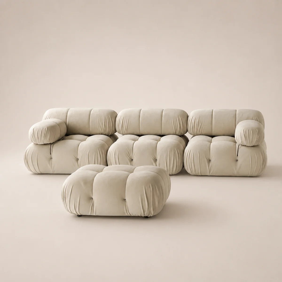 A modular tufted sofa set in a warm off-white or cream bouclé fabric, including a low ottoman in front of a three-seater sofa, photographed in a minimalist studio setting with a matching beige background.