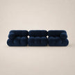 A modern modular sofa upholstered in deep steel blue velvet, composed of three connected tufted cube sections, set against a solid warm beige background.