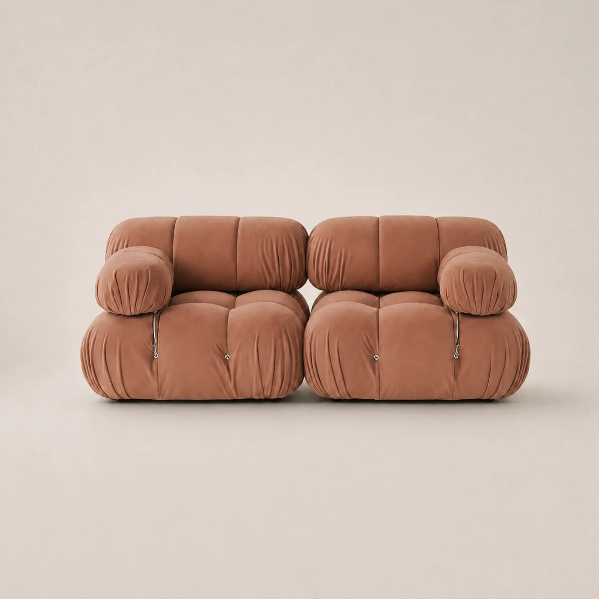 A modern two-seater sofa upholstered in a muted pink velvet fabric, featuring a unique tufted bubble design and small silver metal pull accents on the armrests, set against a solid warm beige background.