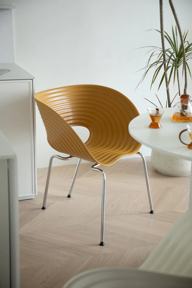 Modern yellow plastic chair in a minimalistic room with a white table and plant.