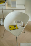 White plastic chair with a yellow object on a wooden floor, with a blurred background of electronic equipment.