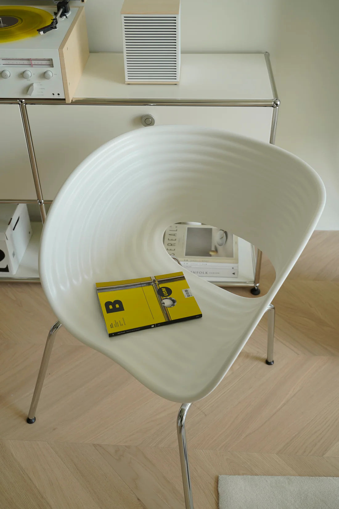 White plastic chair with a yellow object on a wooden floor, with a blurred background of electronic equipment.