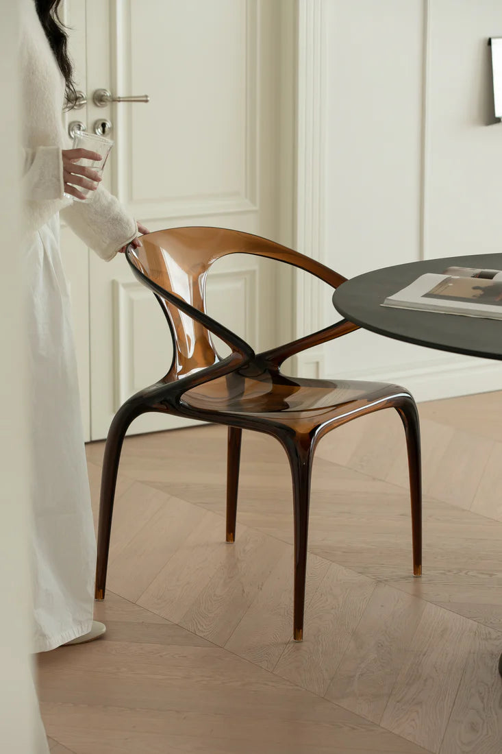 Person holding a modern wooden chair in a minimalistic room with a table and door.
