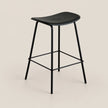 A modern black bar stool with a curved seat, slim metal legs, and a square footrest, shown against a solid light beige background.
