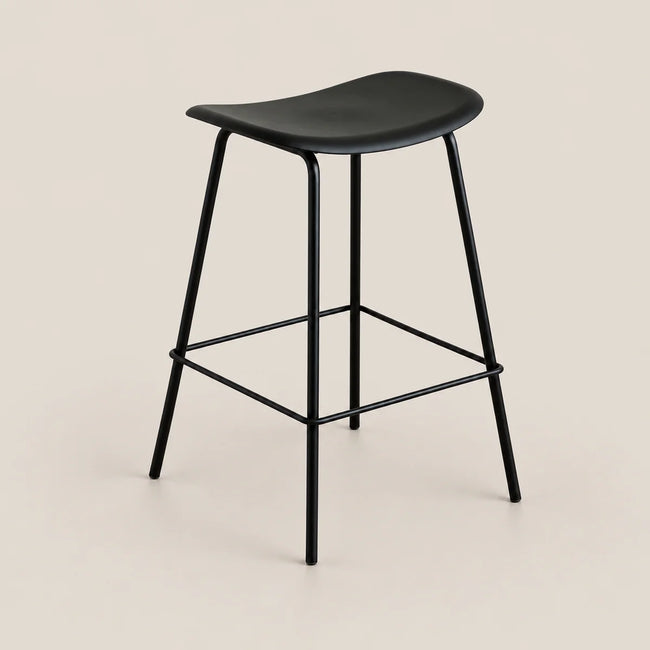 A modern black bar stool with a curved seat, slim metal legs, and a square footrest, shown against a solid light beige background.