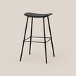 A modern black bar stool with a curved seat, slim metal legs, and a footrest, shown against a solid light beige background.