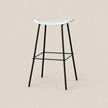 A modern bar stool with a white molded seat and black metal legs, shown against a solid light beige background.