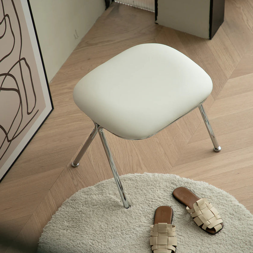 White stool on a wooden floor with a rug and sandals in the foreground