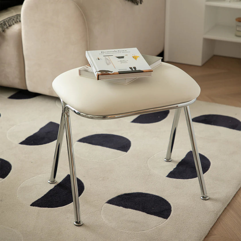 Beige stool with a book on a patterned rug in a living room setting
