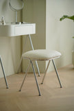 White stool with metal legs in a room with a vanity table and mirror.