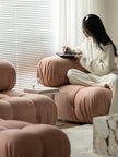 Person sitting on a pink pouf in a modern living room, holding a tablet.