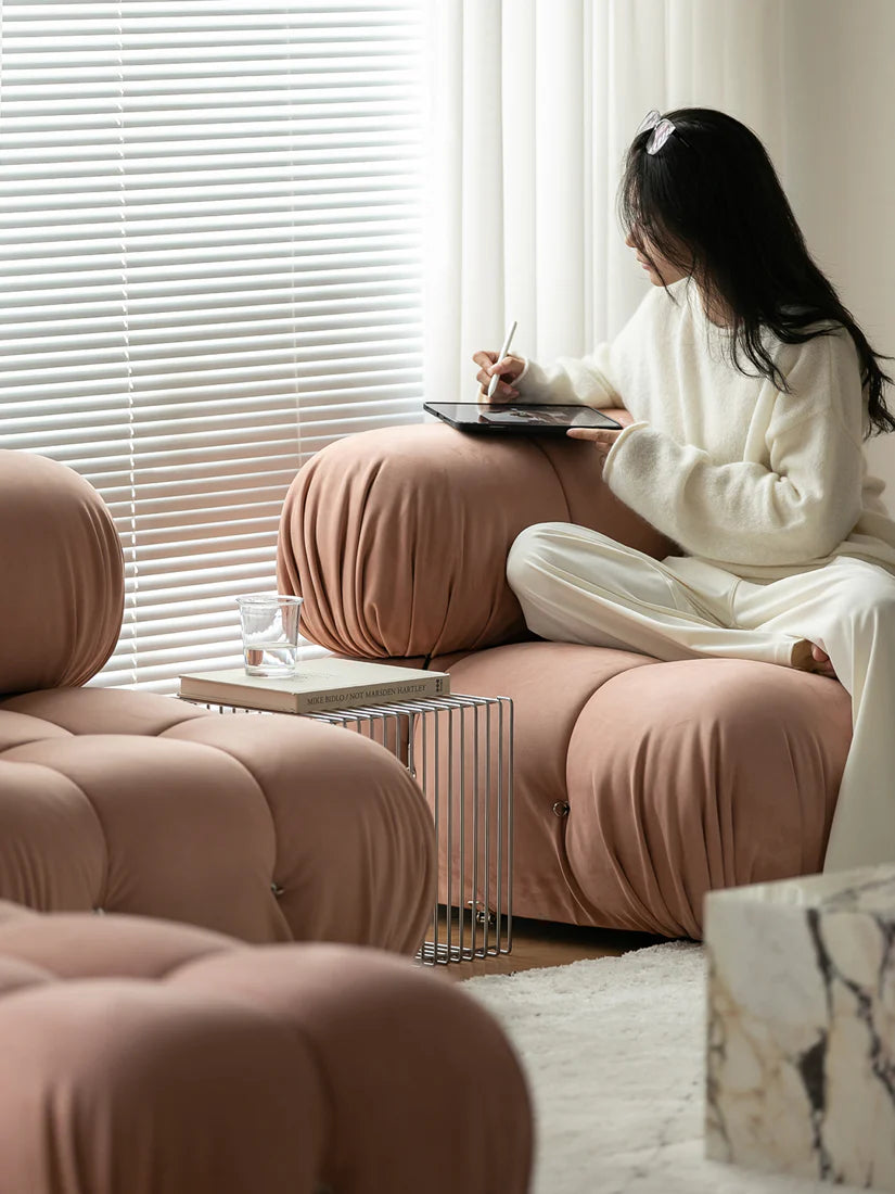 Person sitting on a pink pouf in a modern living room, holding a tablet.