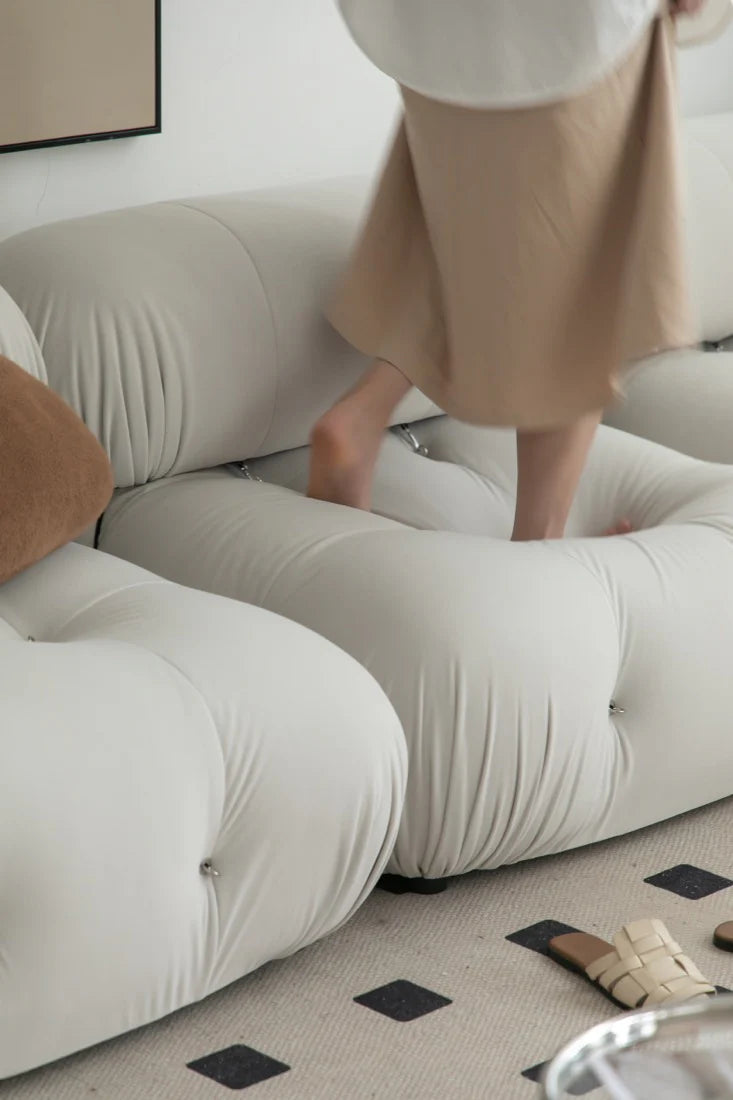 Person wearing a beige skirt standing on a white sofa with a neutral background