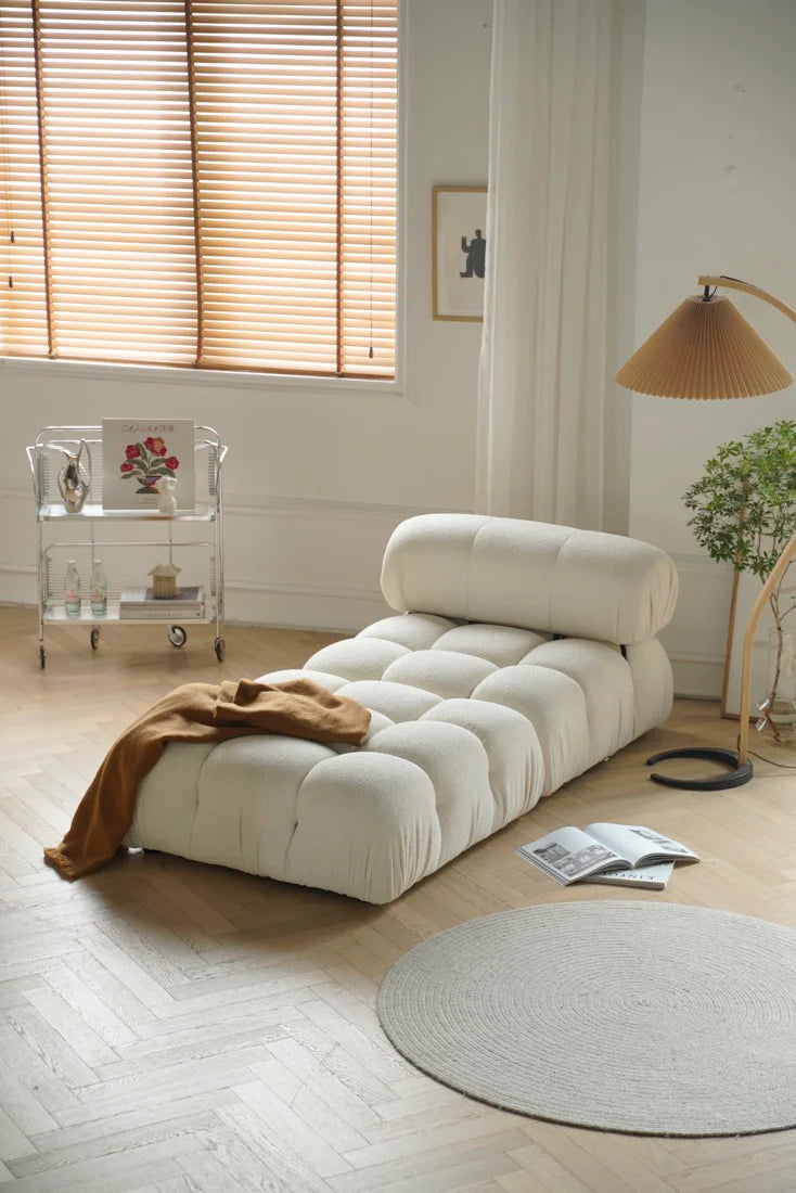 Modern living room with a white sofa, round rug, and window blinds.