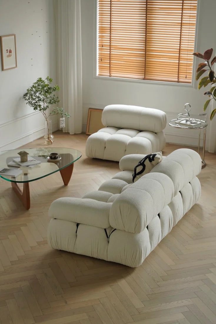 Modern white sofa in a living room with wooden floor and window blinds.