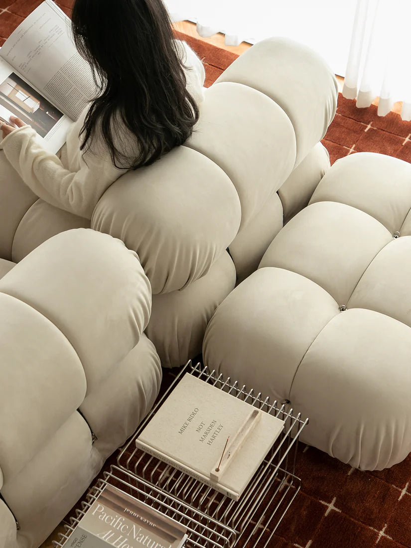Person reading a book on a unique beige cushioned chair with a basket below.