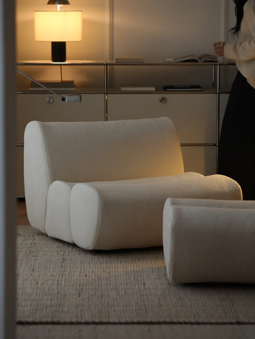 Modern beige armchair in a room with a lamp and reflective surface.