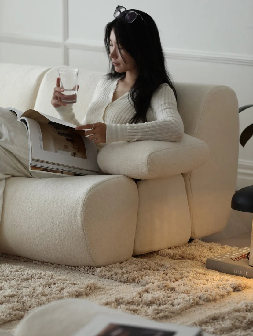 Woman reading a magazine on a beige sofa in a cozy living room.