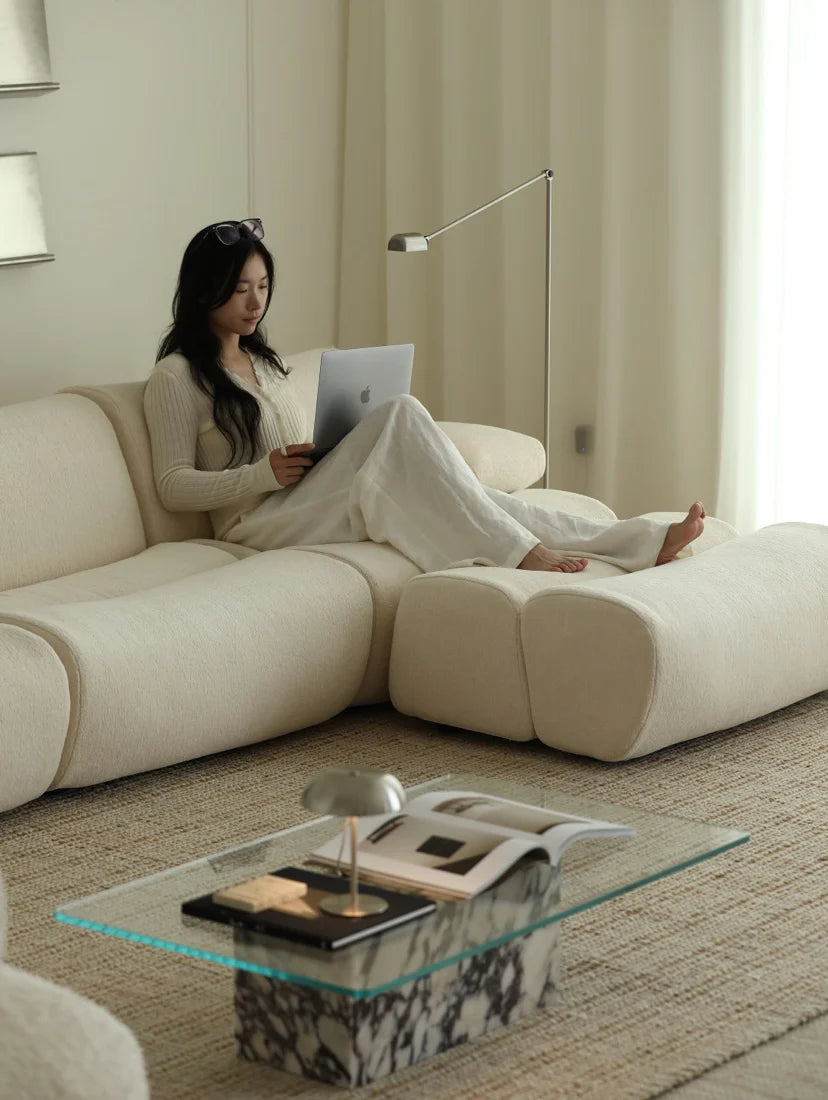 Woman using a laptop on a beige sofa in a modern living room.