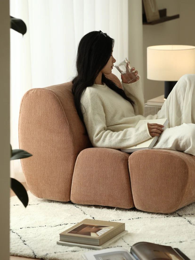 Woman sitting on a brown armchair in a cozy living room, holding a glass.