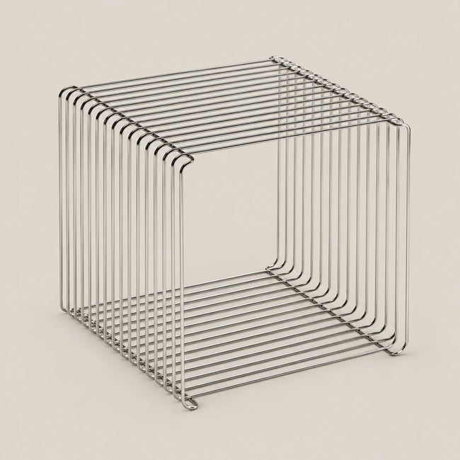 A minimalist, open-frame cube side table made of thin, polished metal wire with a brushed silver finish, set against a solid, warm off-white background.