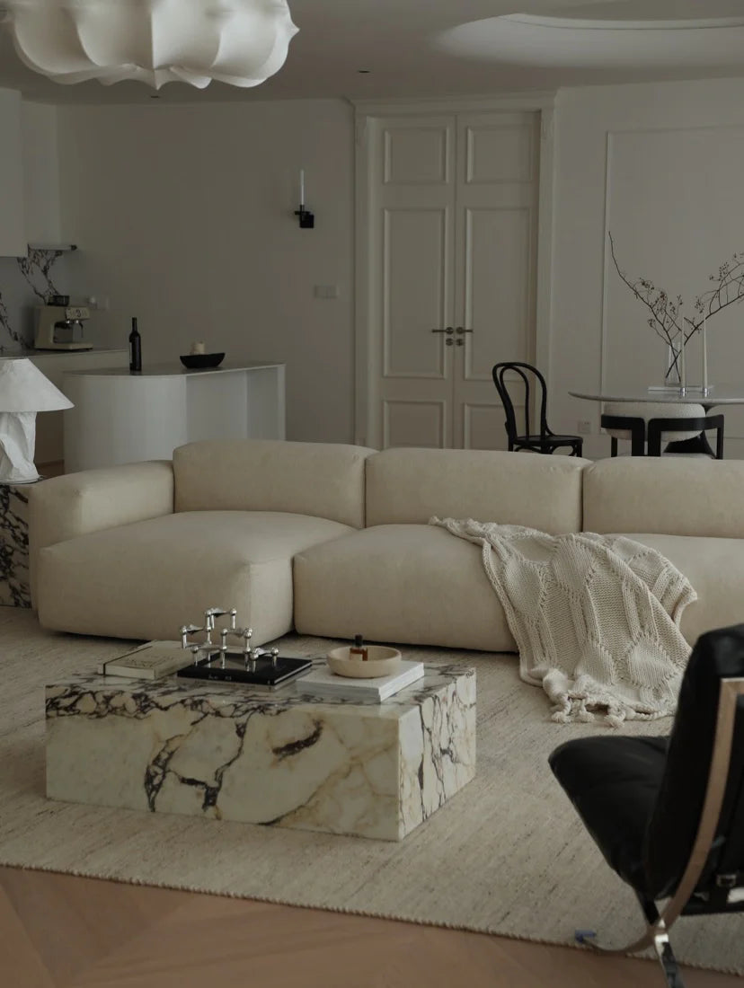 Modern living room with a beige sectional sofa, marble coffee table, and white walls.