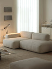Modern living room with a beige sectional sofa, glass coffee table, and decorative items.