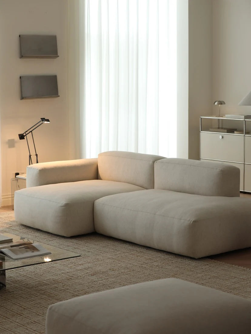 Modern living room with a beige sectional sofa, glass coffee table, and decorative items.