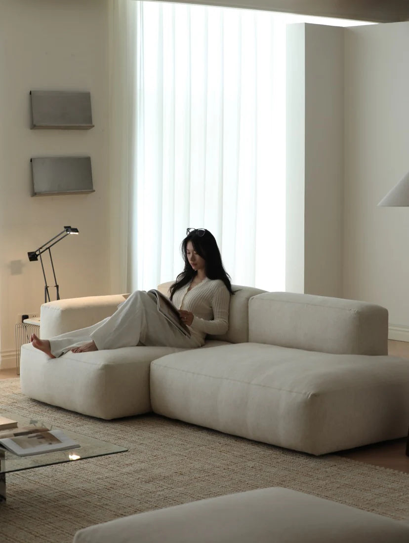 Woman sitting on a modern beige sofa in a minimalistic living room.