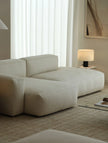 Beige sectional sofa in a living room with a lamp and window blinds.