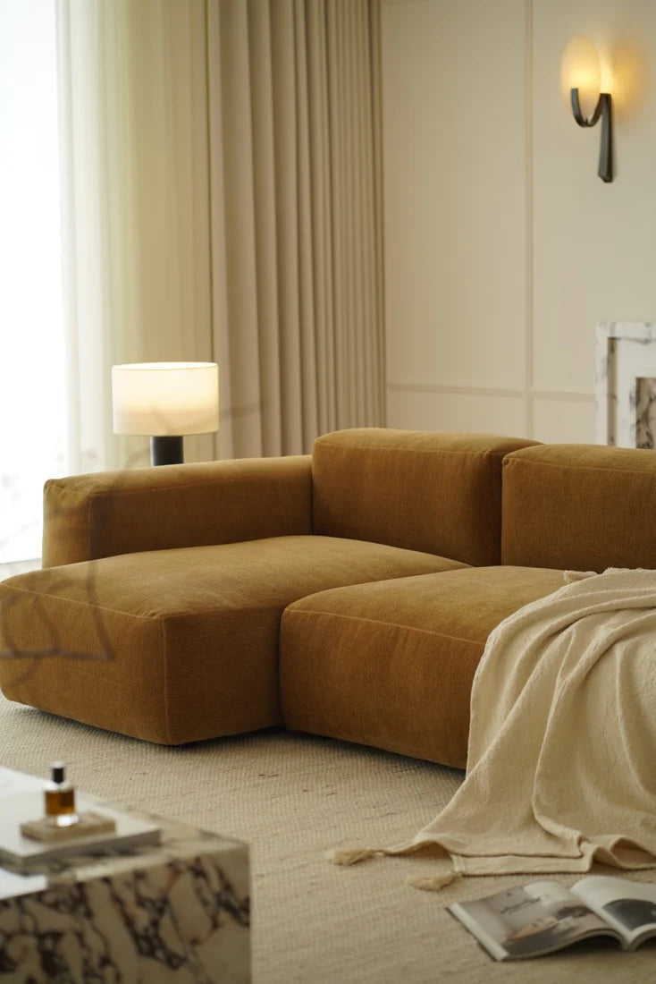 Brown sectional sofa in a living room with a lamp and book on a table.