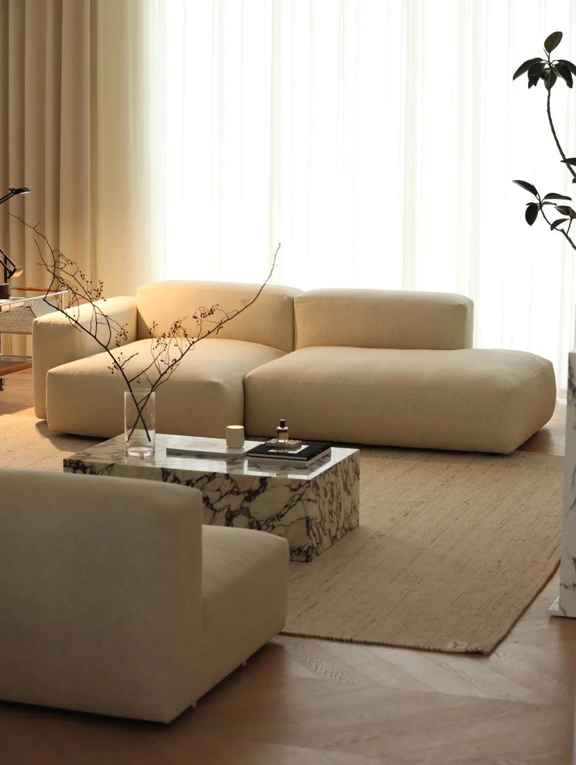 Modern living room with beige sectional sofa and marble coffee table.