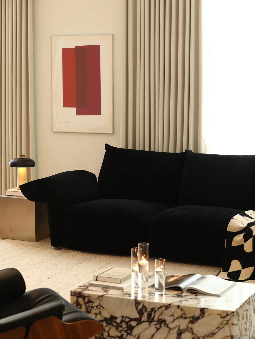 Modern living room with a black sofa, marble coffee table, and abstract art on the wall.