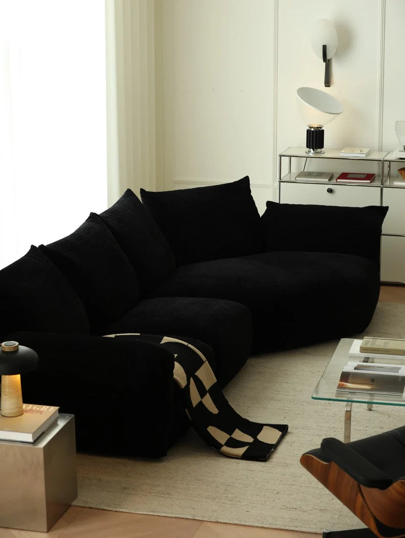 Black sectional sofa in a modern living room with a checkered blanket.
