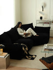 Woman reading a magazine on a black sofa in a modern living room.
